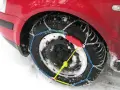 Ecco come mettere le catene da neve: una ruota di un'auto rossa coperta di neve con catene montate.