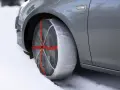 Calze da neve omologate in Italia montate su un'auto grigia su strada innevata.