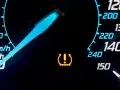 Cruscotto auto con spia pressione gomme accesa. L'indicatore giallo segnala un problema, forse un pneumatico sgonfio.
