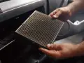 Mani che estraggono un filtro abitacolo sporco, suggerendo la necessità di cambiarlo.