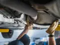 Mani guantate lavorano sul catalizzatore di una macchina, riparando il sistema di scarico.