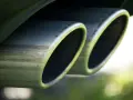Doppi terminali cromati dell'impianto di scarico di un'auto, con riflessi verdi e sfocati sullo sfondo.
