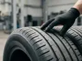 Mano guantata esamina il battistrada di pneumatici, evidenziando la differenza gomme estive e invernali per la sicurezza stradale.