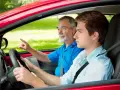 Un giovane neopatentato al volante, con un accompagnatore anziano che indica la strada.