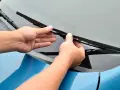 Mani che sostituiscono un tergicristallo sul parabrezza di un'auto blu. Guida rapida su come cambiare tergicristalli.