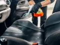 Mani guantate spruzzano detergente sul sedile dell'auto per pulire vomito.