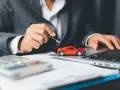 Persona in giacca grigia analizza costi auto con calcolatrice e laptop, accanto a un modellino rosso. Si chiede ogni quanto si paga il bollo auto.