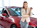 Donna sorridente con le chiavi in mano, accanto a una nuova auto rossa, pronta per il rodaggio.