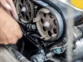 Mano che lavora sul motore, ingranaggi e cinghia di distribuzione. Scopri quanto costa cambiare la cinghia di distribuzione per la tua auto.