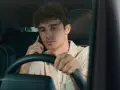 Giovane uomo al volante con il cellulare all'orecchio, distratto dalla conversazione.