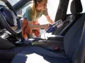Donna usa un aspirapolvere portatile per pulire i sedili dell'auto, rimuovendo polvere e briciole per un interno impeccabile.
