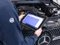 Meccanico usa tablet per diagnosi auto. Il display mostra icone per controlli e manutenzione, suggerendo quanto dura la revisione auto.