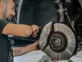 Meccanico sorridente effettua manutenzione a3 Mercedes, concentrato sul freno a disco forato e pinza con logo.