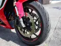 Ruota anteriore di una moto rossa, con disco freno forato e pinza ABS. Il volante che vibra a bassa velocità è un dettaglio che si percepisce.