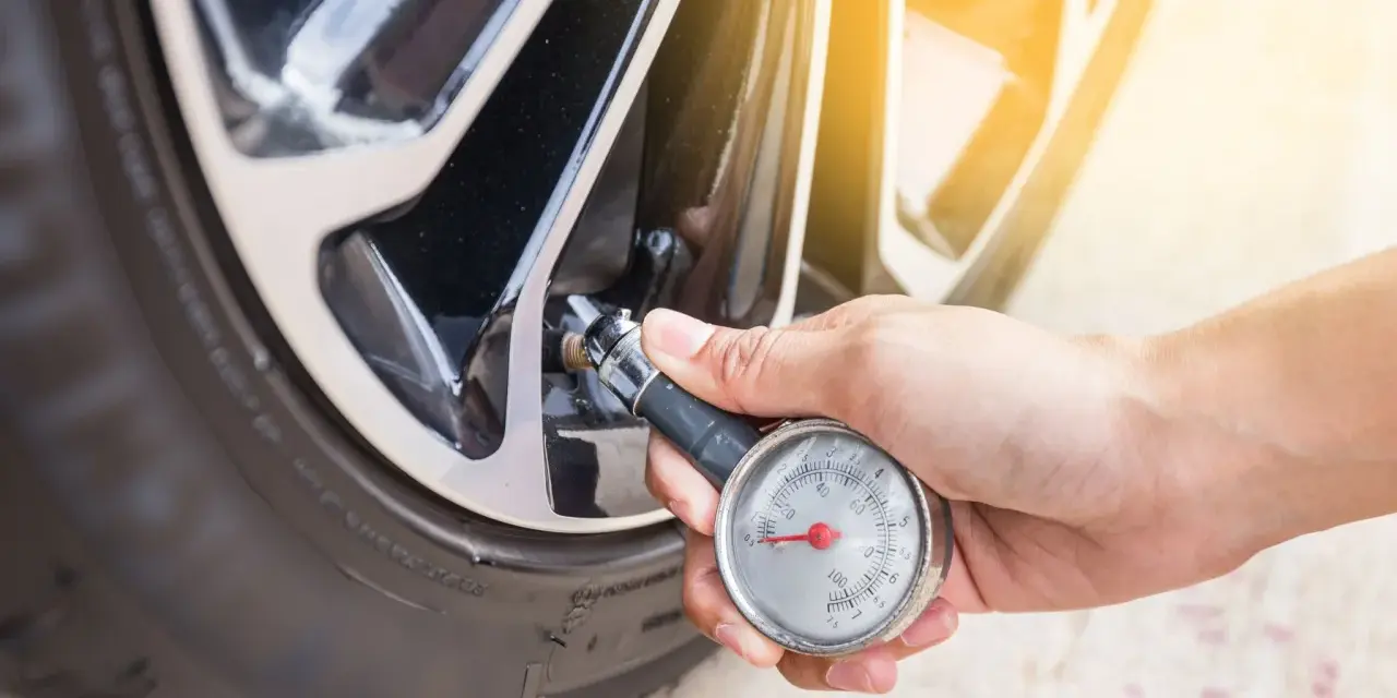 Controllo della pressione gomme auto con manometro. La mano tiene lo strumento collegato alla valvola del pneumatico.