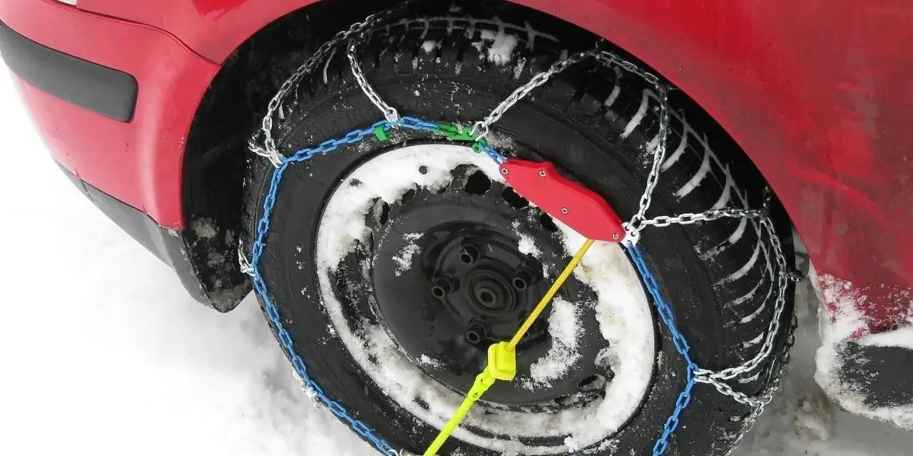 Ecco come mettere le catene da neve: una ruota di un'auto rossa coperta di neve con catene montate.