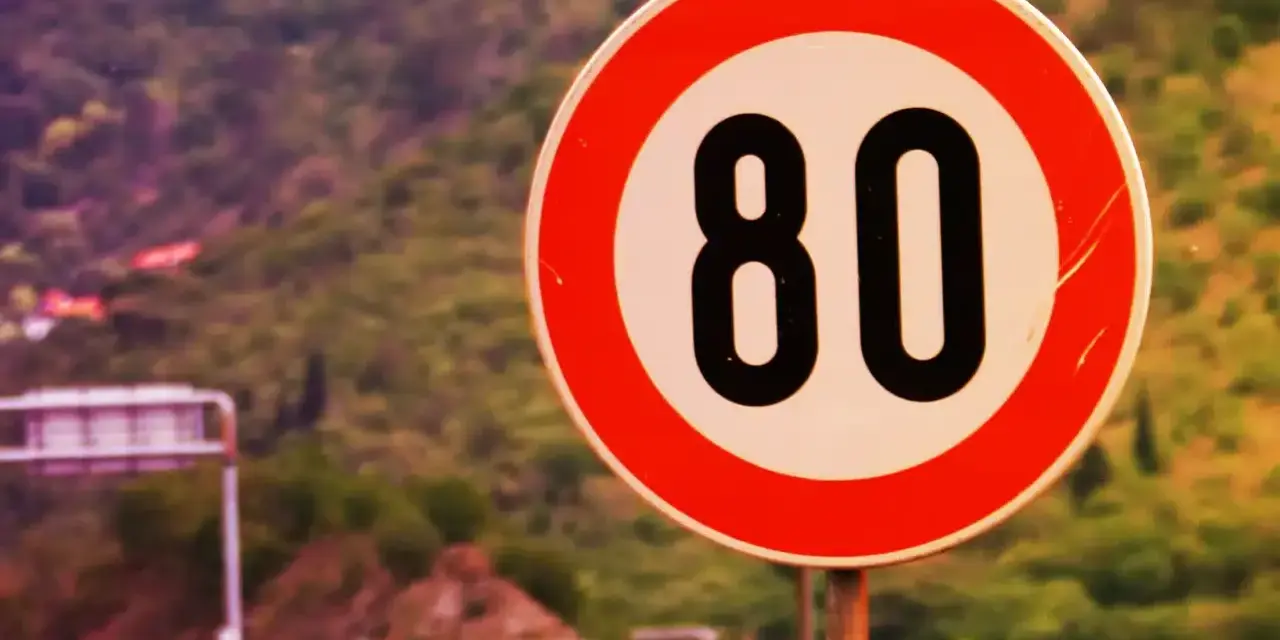 Segnale di limite massimo nei centri abitati: 80 km/h. Strada panoramica con vegetazione sullo sfondo.