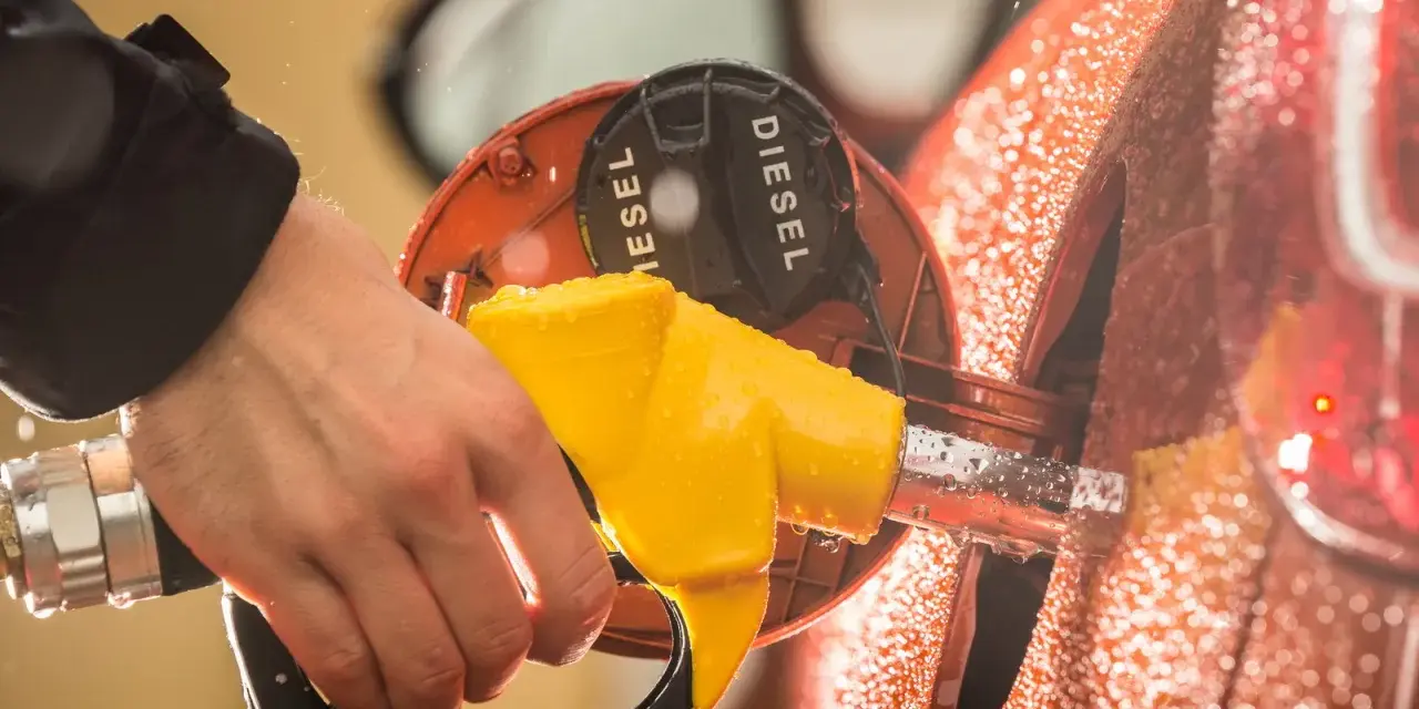 Mano che inserisce la pompa del **diesel nella benzina**. Gocce d'acqua sulla carrozzeria arancione.