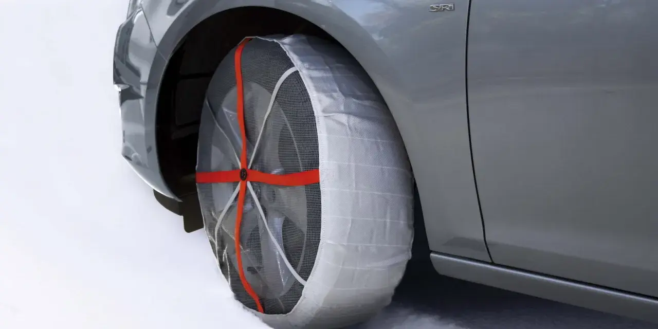 Calze da neve omologate in Italia montate su un'auto grigia su strada innevata.