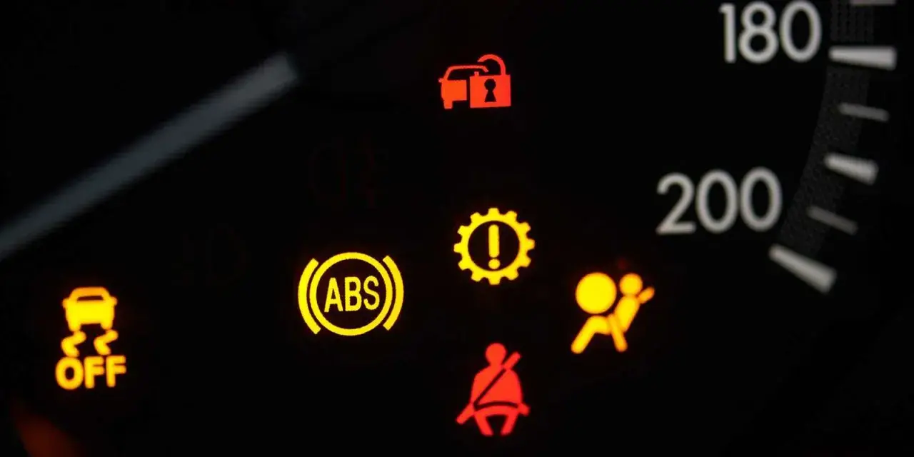 Cruscotto auto con spia ABS e freno a mano accese, insieme ad altre spie di avaria.