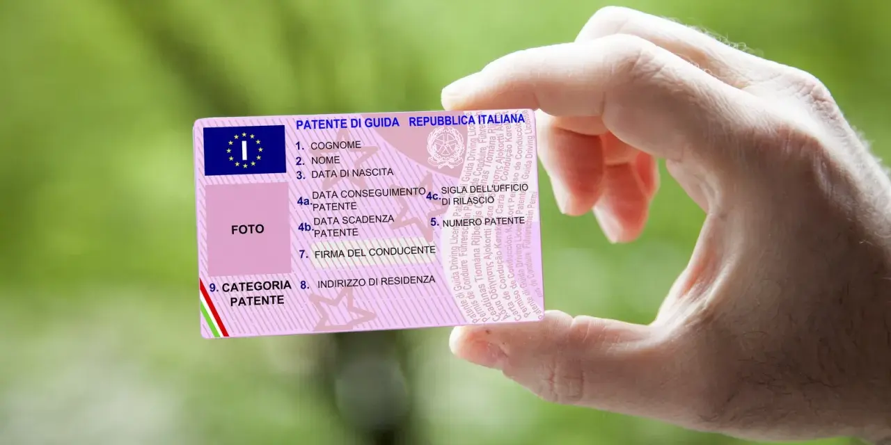 Mano che tiene una patente italiana, con dettagli su nome, data di nascita e scadenza. Nuove regole patente in arrivo?