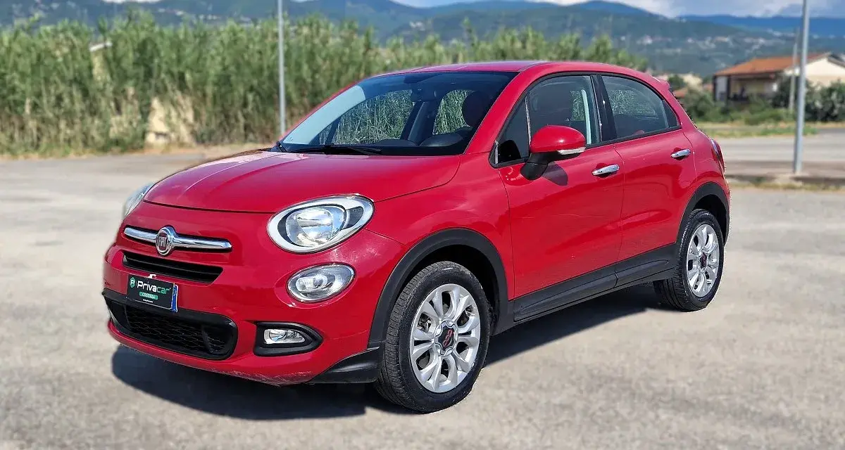 Fiat 500X rossa parcheggiata all'aperto, con montagne sullo sfondo. Controlla la pressione pneumatici per un viaggio sicuro.