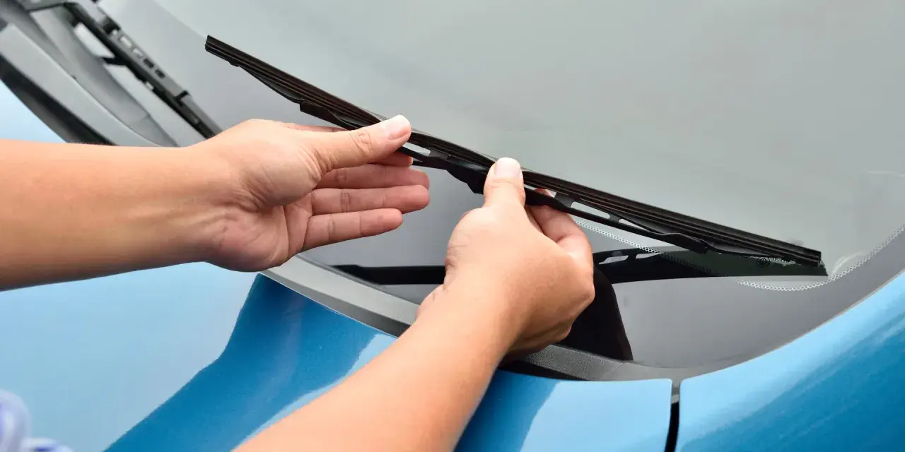 Mani che sostituiscono un tergicristallo sul parabrezza di un'auto blu. Guida rapida su come cambiare tergicristalli.