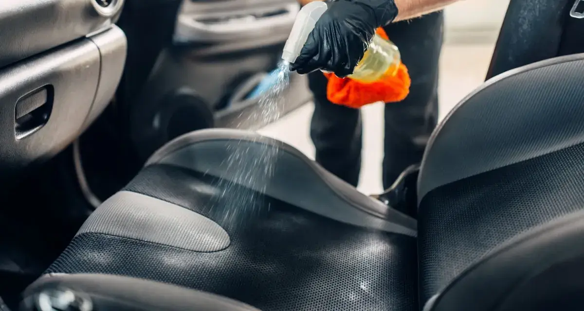 Mani guantate spruzzano detergente sul sedile dell'auto per pulire vomito.