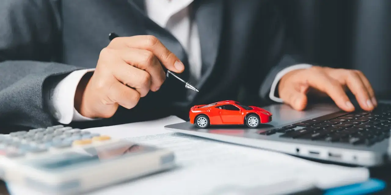 Persona in giacca grigia analizza costi auto con calcolatrice e laptop, accanto a un modellino rosso. Si chiede ogni quanto si paga il bollo auto.