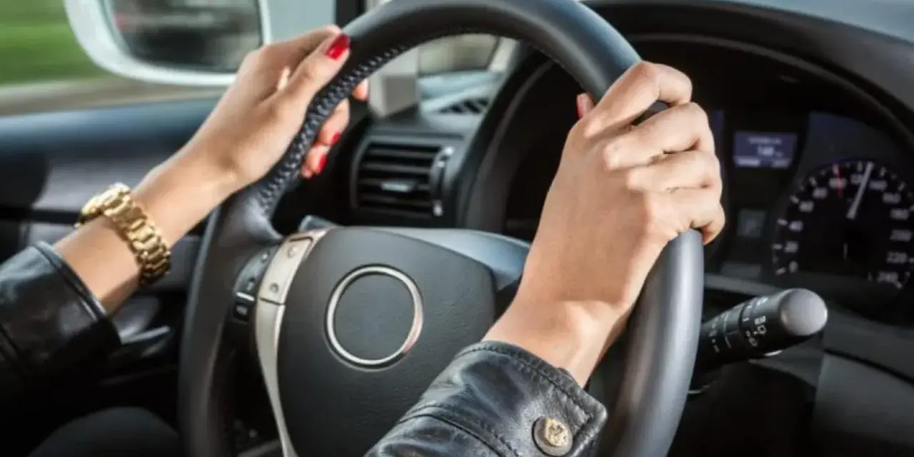Mani con smalto rosso e bracciale d'oro tengono il volante. Il cruscotto mostra la velocità, definendo cosa vuol dire anteriore in un'auto.