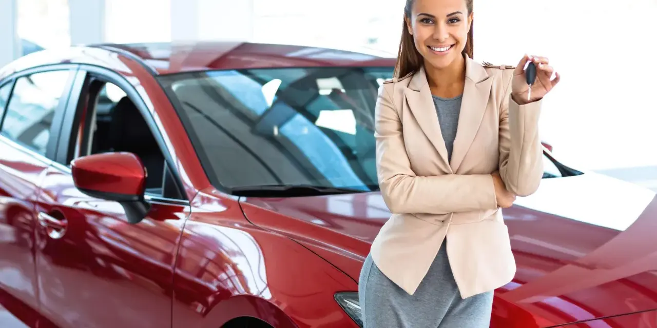 Donna sorridente con le chiavi in mano, accanto a una nuova auto rossa, pronta per il rodaggio.