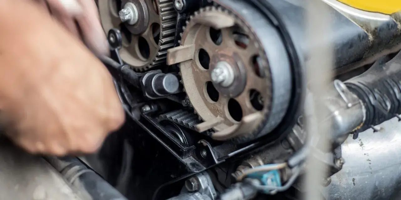 Mano che lavora sul motore, ingranaggi e cinghia di distribuzione. Scopri quanto costa cambiare la cinghia di distribuzione per la tua auto.