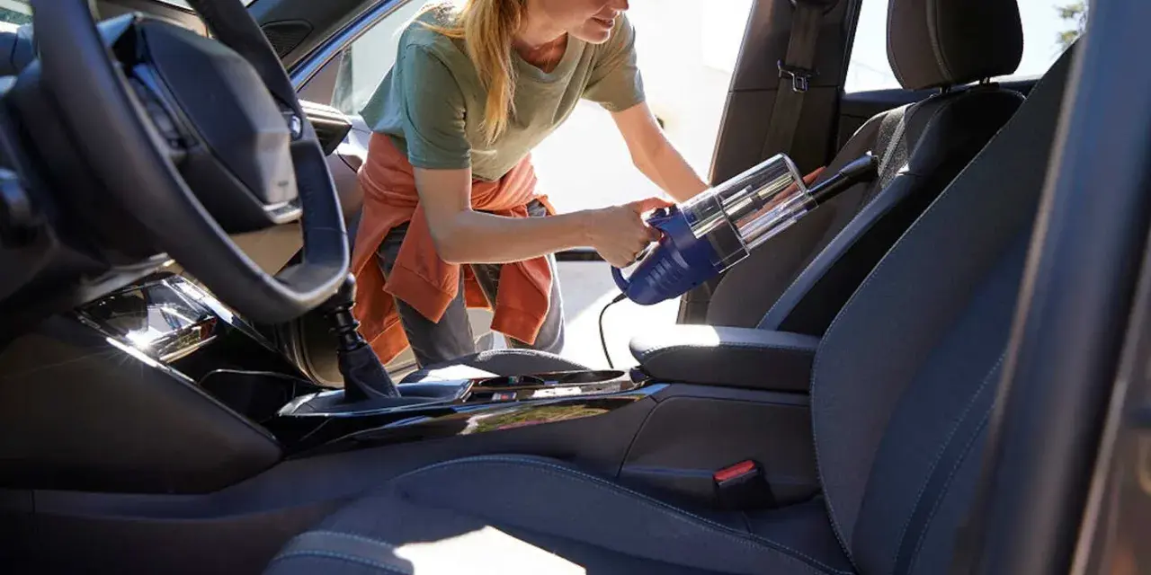 Donna usa un aspirapolvere portatile per pulire i sedili dell'auto, rimuovendo polvere e briciole per un interno impeccabile.