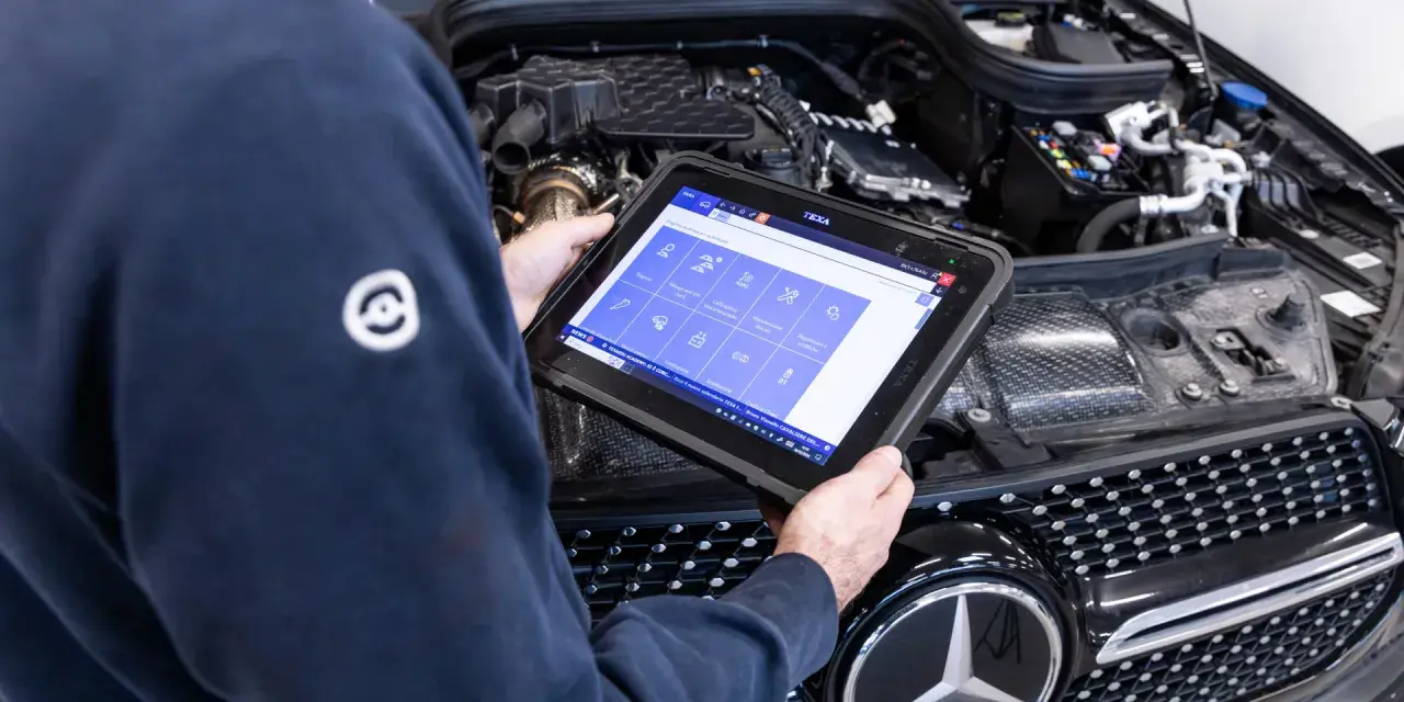 Meccanico usa tablet per diagnosi auto. Il display mostra icone per controlli e manutenzione, suggerendo quanto dura la revisione auto.