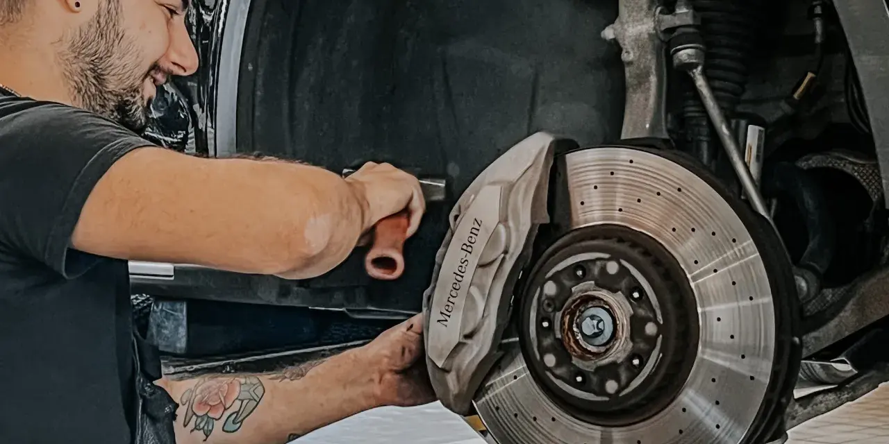 Meccanico sorridente effettua manutenzione a3 Mercedes, concentrato sul freno a disco forato e pinza con logo.