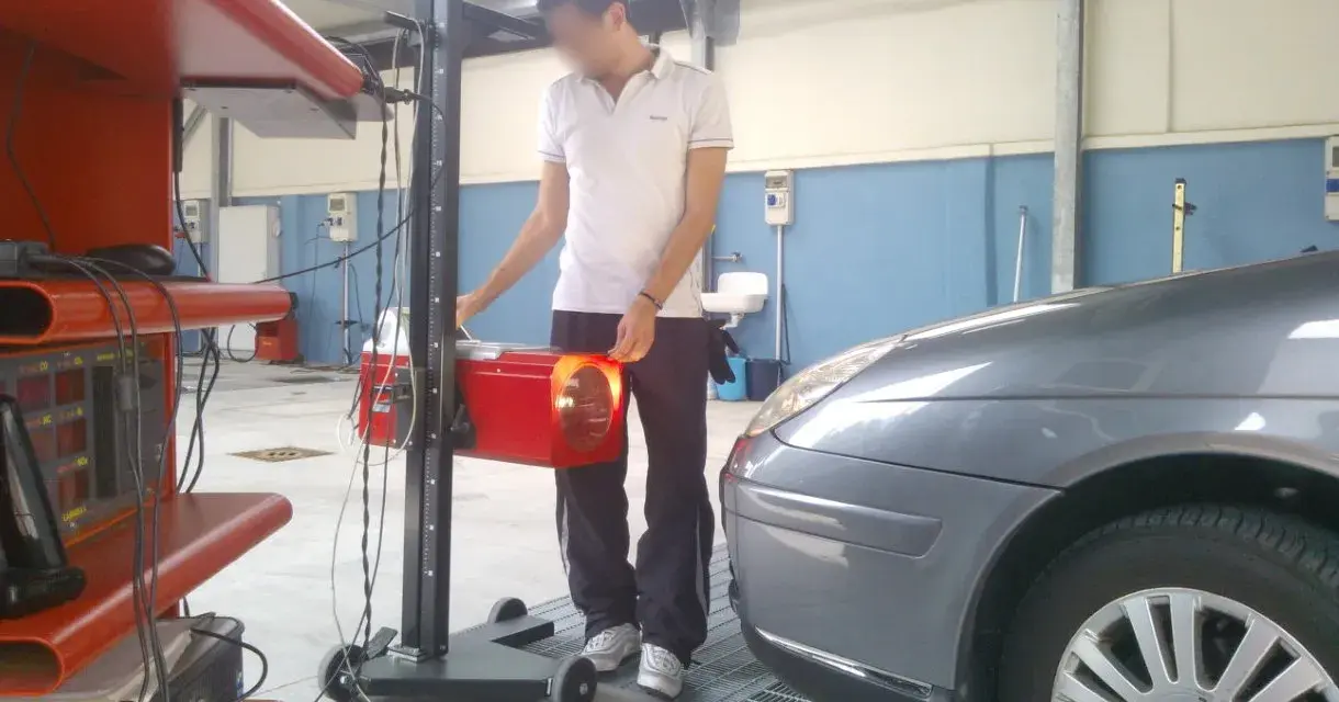 Tecnico effettua la revisione auto ibride in officina, regolando un faro con apparecchiatura specifica.