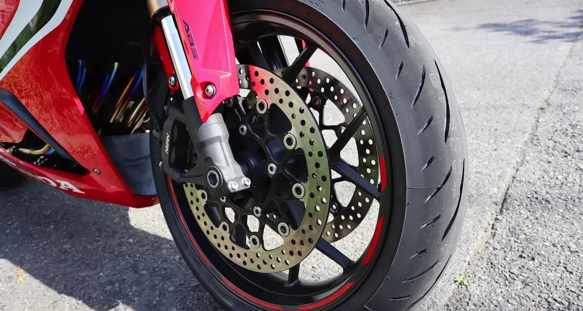 Ruota anteriore di una moto rossa, con disco freno forato e pinza ABS. Il volante che vibra a bassa velocità è un dettaglio che si percepisce.