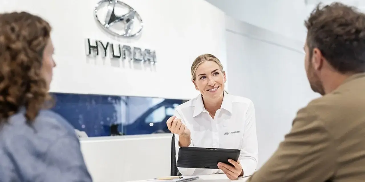 Venditrice Hyundai sorridente mostra un tablet a una coppia, discutendo il tagliando della loro auto.