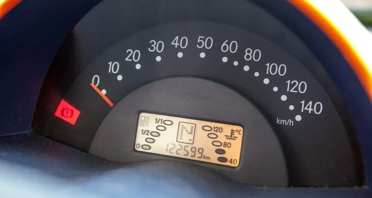 Cruscotto auto con tachimetro e spia del freno di stazionamento accesa. Chilometraggio 122599 km.