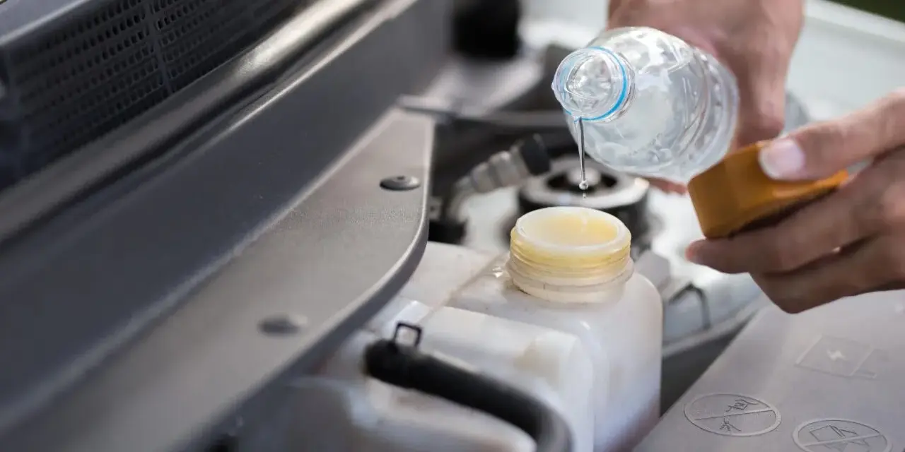Mani versano acqua distillata nel serbatoio del radiatore dell'auto, un gesto di cura per il motore.