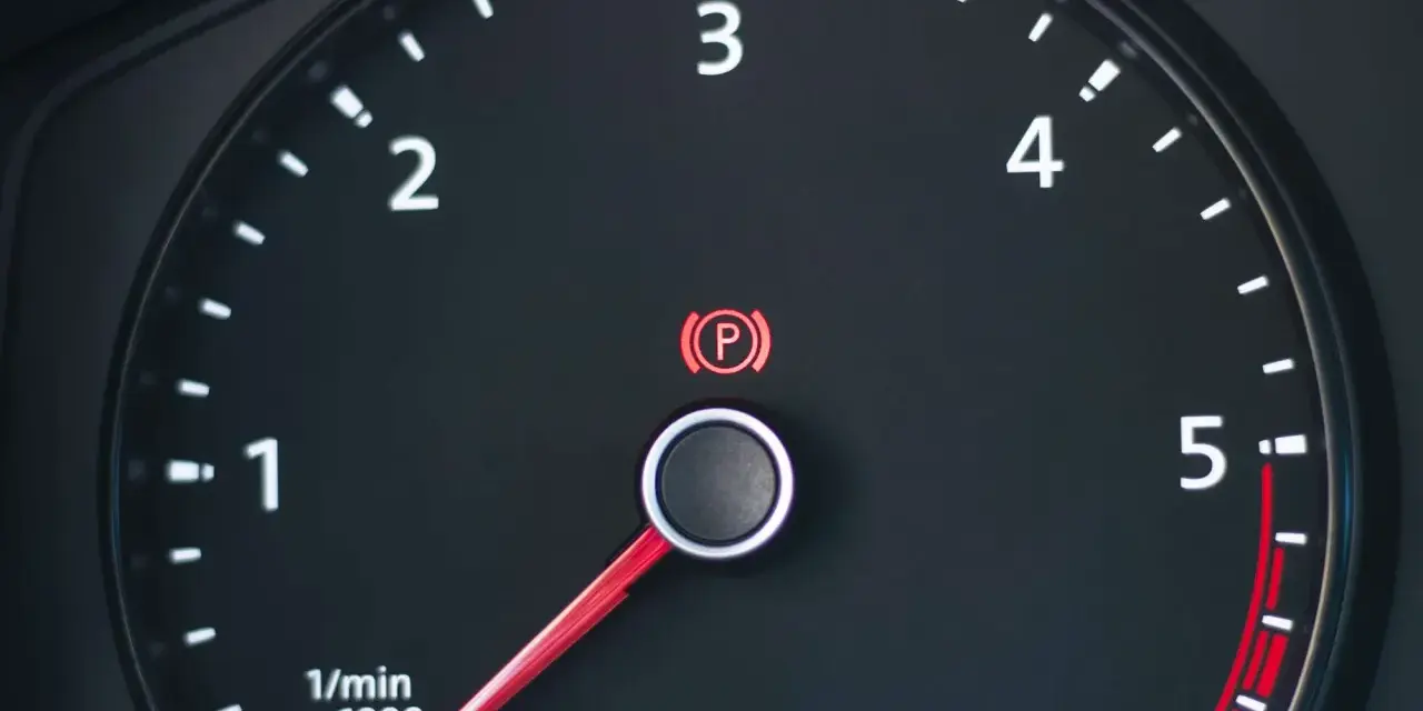Cruscotto auto con tachimetro e spia freno a mano accesa.