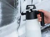Mano che spruzza schiuma per lavare auto a casa con un erogatore.