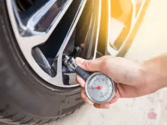 Controllo della pressione gomme auto con manometro. La mano tiene lo strumento collegato alla valvola del pneumatico.