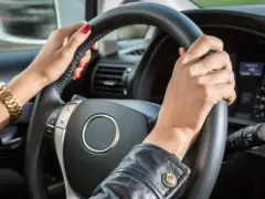 Mani con smalto rosso e bracciale d'oro tengono il volante. Il cruscotto mostra la velocità, definendo cosa vuol dire anteriore in un'auto.