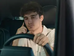 Giovane uomo al volante con il cellulare all'orecchio, distratto dalla conversazione.