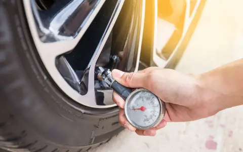 Controllo della pressione gomme auto con manometro. La mano tiene lo strumento collegato alla valvola del pneumatico.