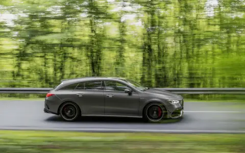 Un'auto sportiva grigia sfreccia su una strada, con gli alberi verdi sfocati sullo sfondo. Il freno motore è pronto per ogni curva.