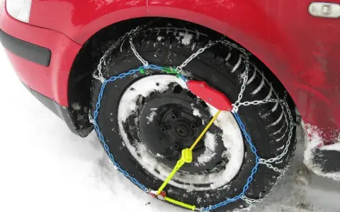 Ecco come mettere le catene da neve: una ruota di un'auto rossa coperta di neve con catene montate.