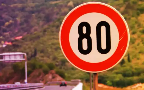 Segnale di limite massimo nei centri abitati: 80 km/h. Strada panoramica con vegetazione sullo sfondo.