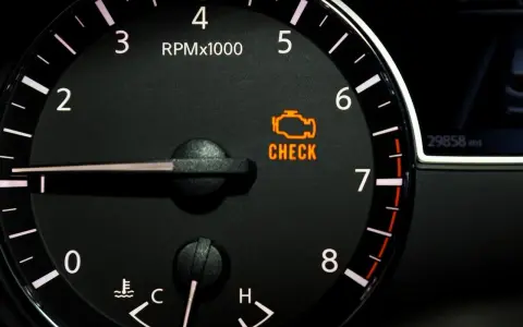 Cruscotto auto con tachimetro e spia gialla motore accesa. Indica un problema da controllare.